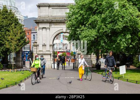 Personen mit Fahrrädern, die Gesichtsmasken tragen, betreten den St.Stephen`s Green Park in Dublin, der während der COVID-19-Pandemie die sozialen Distanzierungsregeln einhält. Stockfoto